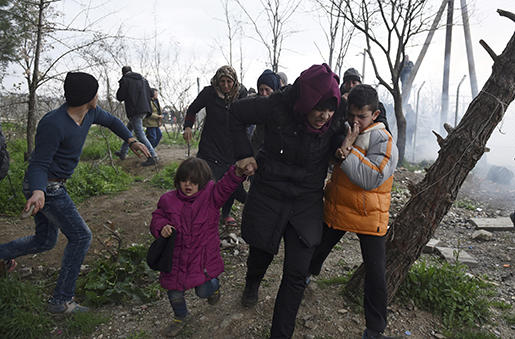 En kvinna flyr med sina barn, sedan makedonsk polis avfyrat tårgas över gränsen vid Idomeni. Minst 6 500 migranter väntar på att passera. Foto: AP Photo/Giannis Papanikos