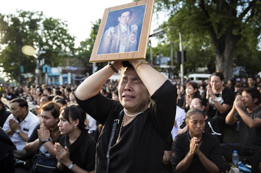 A Thai woman cries as she holds a picture of the late King Bhumibol Adulyadej as others clasp their hands to pay their last respect to a passing van carrying the body of their king outside Grand Palace in Bangkok, Thailand Friday, Oct. 14, 2016. Bhumibol, the world's longest reigning monarch, died on Thursday at the age of 88. (AP Photo/Wason Wanichakorn)