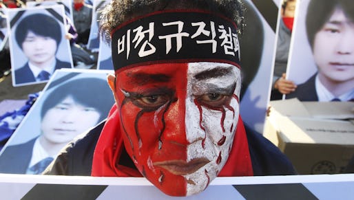 A worker with his face painted, stands in front of portraits of Choi Jong-beom as he participates in a rally against government's labor policy in front of the Seoul City Hall in Seoul, South Korea, Sunday, Nov. 10, 2013. About 20,000 members of the Korean Confederation of Trade Union demanded better working condition and the end to companies' use of temporary employees. Choi Jong-beom was a Samsung Electronics Service employee, who reportedly killed himself after leaving a message complaining about harsh working conditions. The headband reads "Abolition of temporary employees." (AP Photo/Ahn Young-joon)