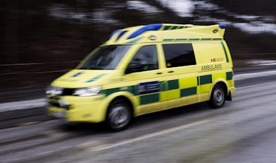 En gul och grön ambulans kör snabbt på en väg med lätt snötäcke.