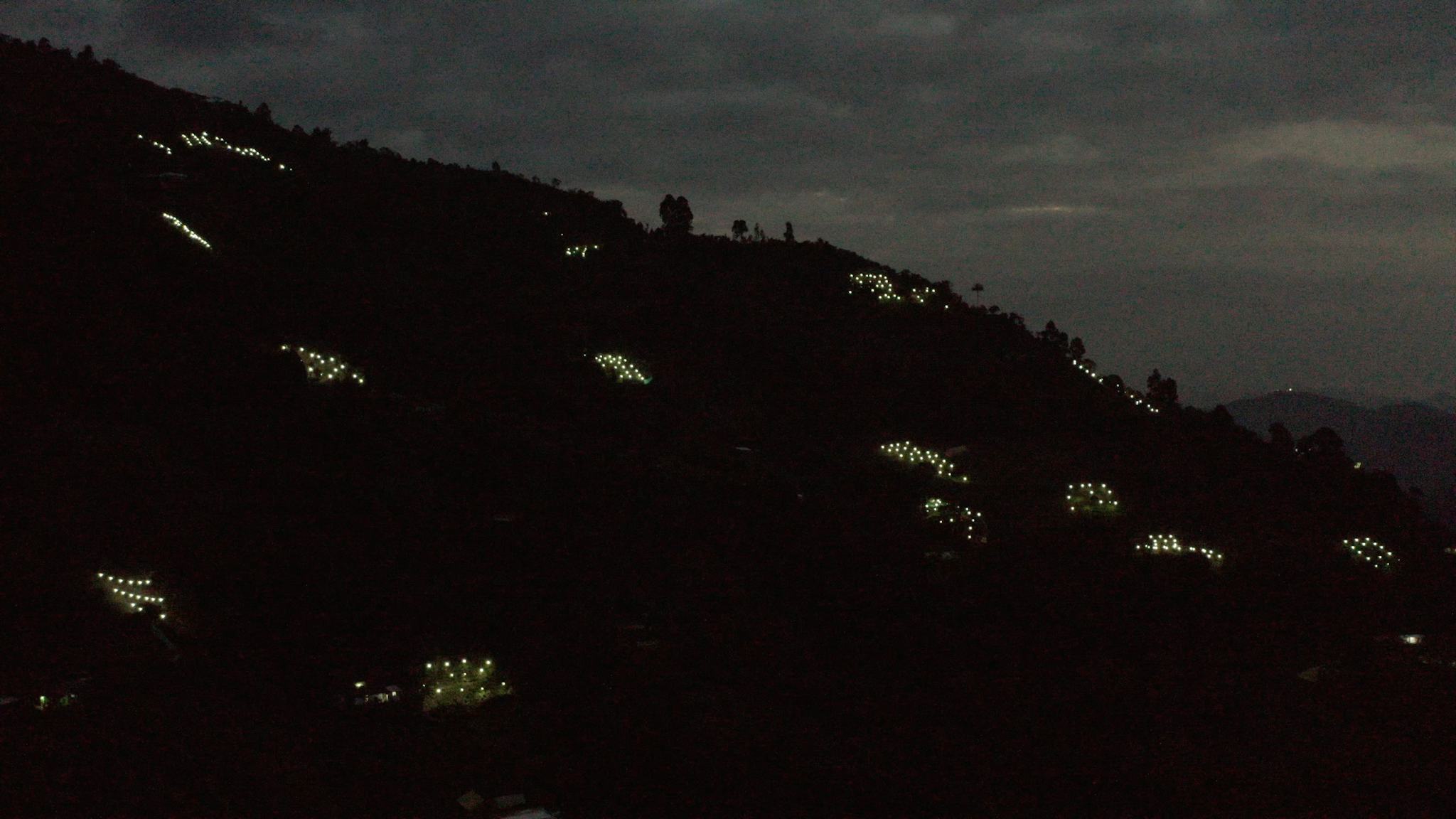 Små kluster av ljus syns utspridda på en bergssluttning. Det är lampor för odlingar av koka och marijuana. I bakgrunden syns en mörk natthimmel.