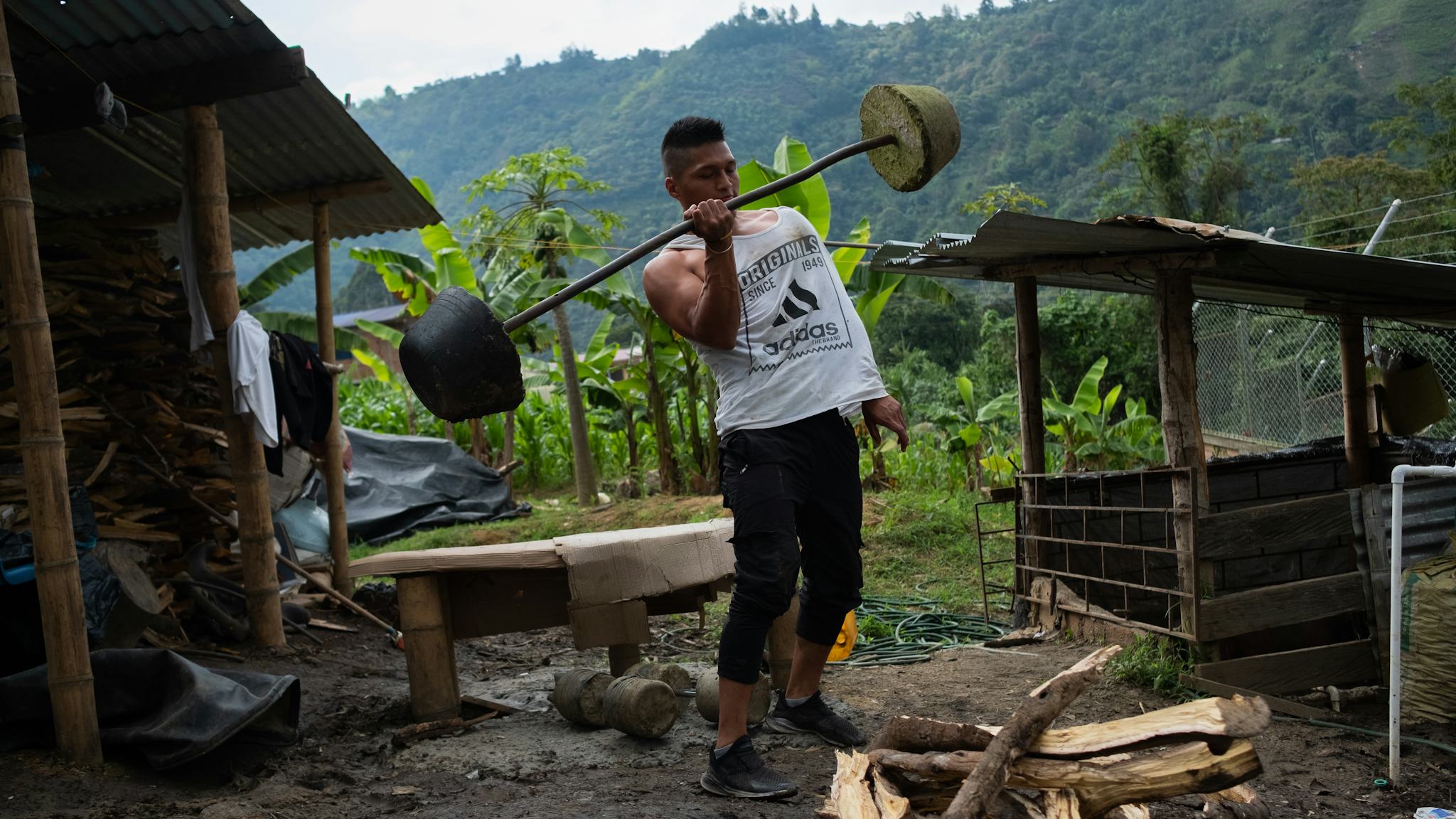 En ung man tränar på gården till ursprungsfolket Nasas huvudkontor. Han är muskulös, klädd i vitt linne och lyfter en hemmabyggd skivstång med ena handen.