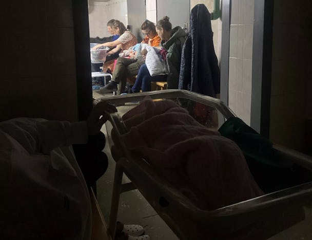 Tre mammor och en pappa sitter med sina barn i ett skyddsrum till ett BB i Kiev. I förgrunden, i mörkret, syns en barnsäng.