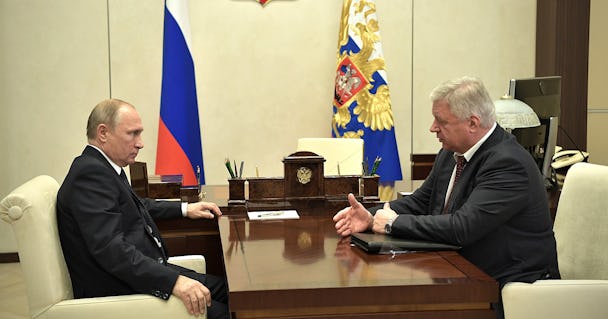 Rysslands president Vladimir Putin, till vänster, och den ryska fackliga federationen FNPR:s ordförande Mikhail Shmakov, till höger, konverserar över ett brunt träbord, sitter i vita fåtöljer, mot en vit vägg i bakgrunden hänger två ryska flaggor.