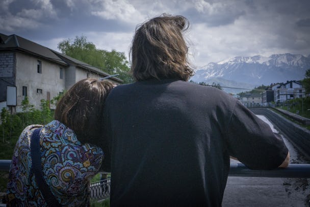 En man och en kvinna står med ryggarna vända mot kameran. Kvinnan lutar huvudet mot mannens axel. I bakgrunden syns berg med snötäckta toppar.