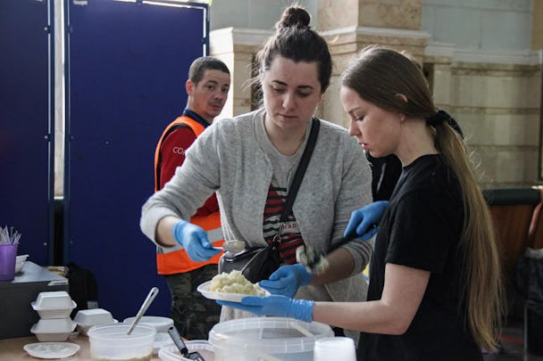 Två volontärer på Kievs centralstation fyller en tallrik med mat till flyktingar.