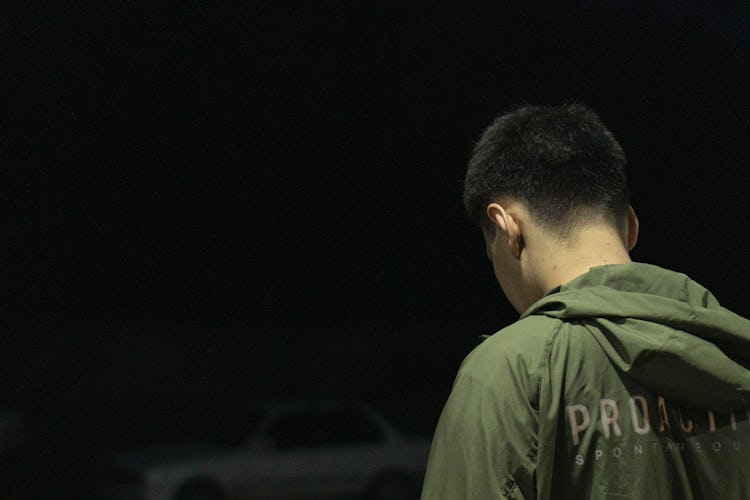 En ung mörkhårig man i grön jacka står med ansiktet vänt bort från kameran. Det är natt och utomhus.