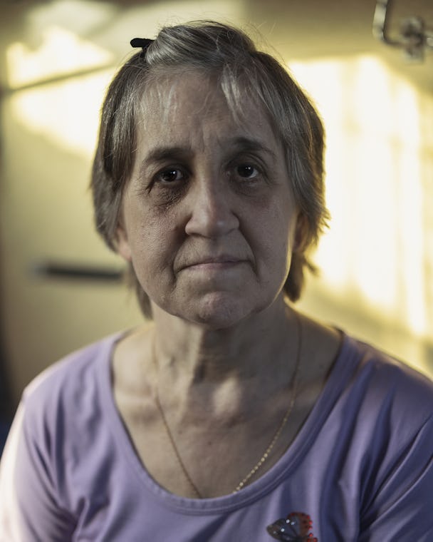 En gråhårig medelålders kvinna i ljuslila tröja tittar in i kameran. 