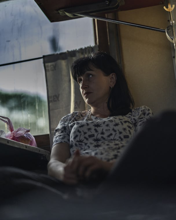 En mörkhårig kvinna i 40-årsåldern, i ljus t-tröja med mönster, sitter på en brits i en tågkupé med ryggen lutad mot väggen.