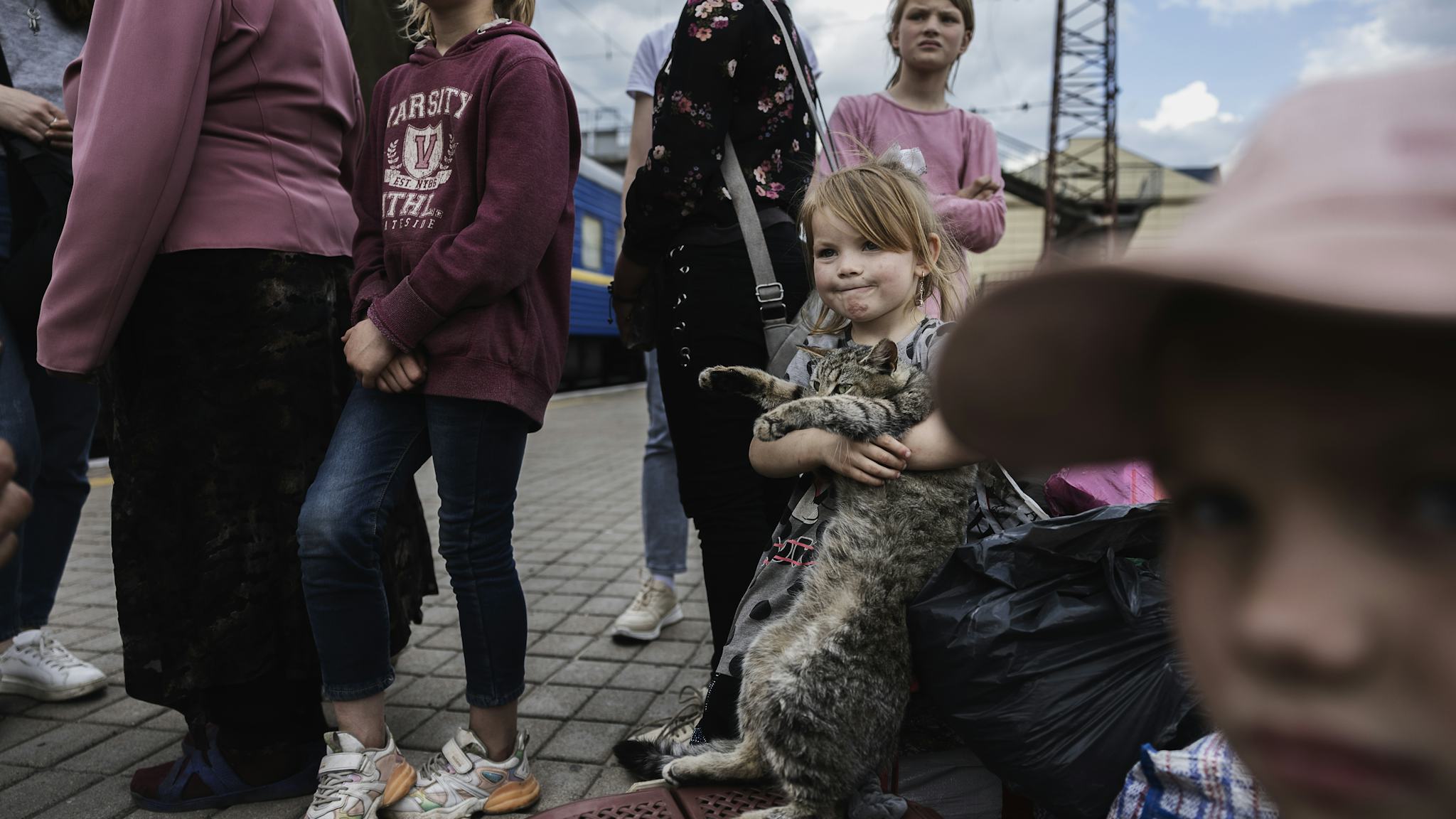 En liten flicka lyfter en katt i famnen på en tågperrong. Runt om henne står äldre syskon.