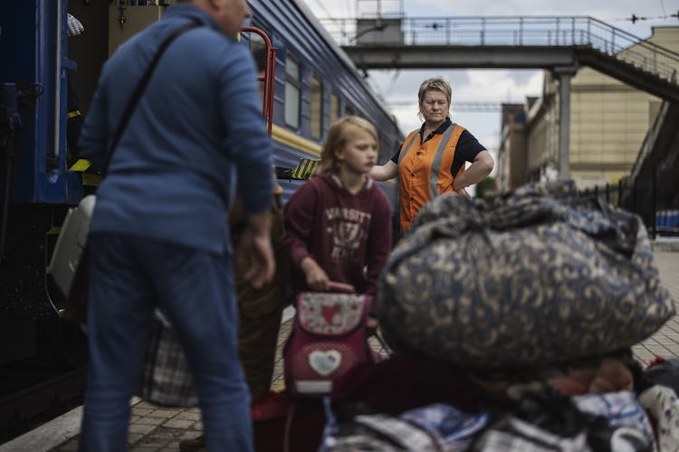 En blond medelålders kvinna från järnvägsbolaget ser på medan flyktingar lastar ombord sina väskor på tåget.