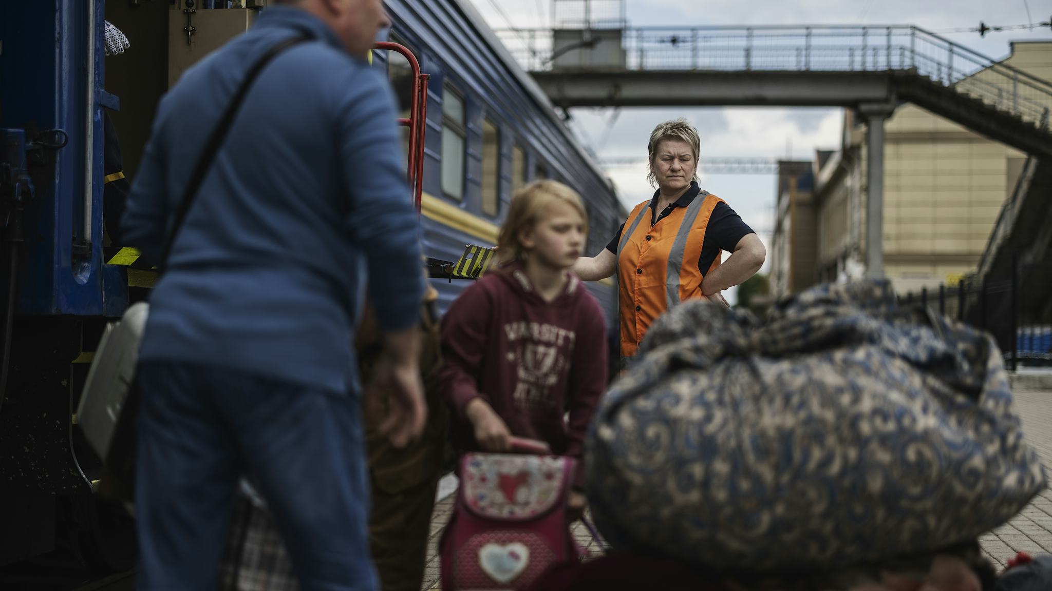 En blond medelålders kvinna från järnvägsbolaget ser på medan flyktingar lastar ombord sina väskor på tåget.
