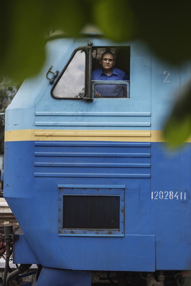 En lokförare tittar ut genom ett fönster från ett blått ukrainskt tåg.