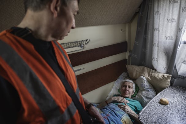 En läkare i orange väst pratar med en äldre kvinna som ligger på en slaf i en tågkupé.