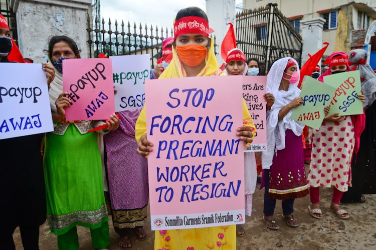 En grupp kvinnliga textilarbetare i Bangladesh håller upp skyltar med protestbudskap. De bär ansiktsmasker.