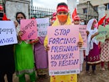 En grupp kvinnliga textilarbetare i Bangladesh håller upp skyltar med protestbudskap. De bär ansiktsmasker.