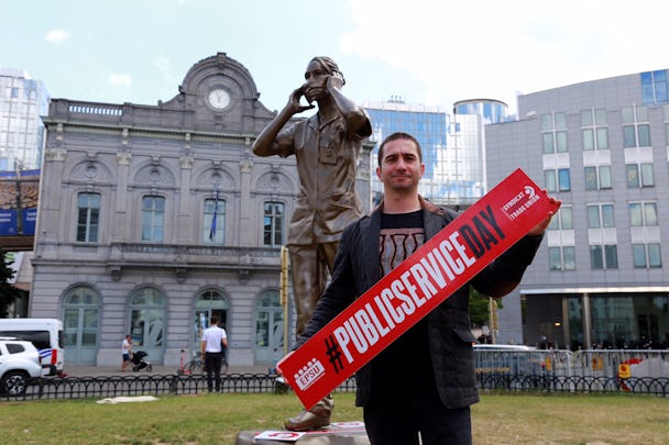 En svartklädd man håller upp en röd banderoll, i bakgrunden syns en staty. 