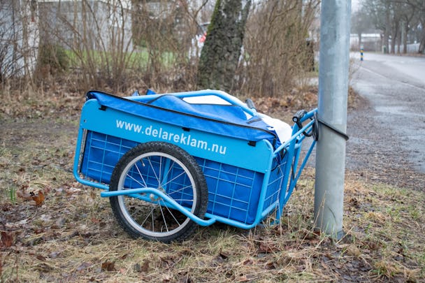 En blå vagn med texten www.delareklam.nu på, fastlåst vid en lamppost.