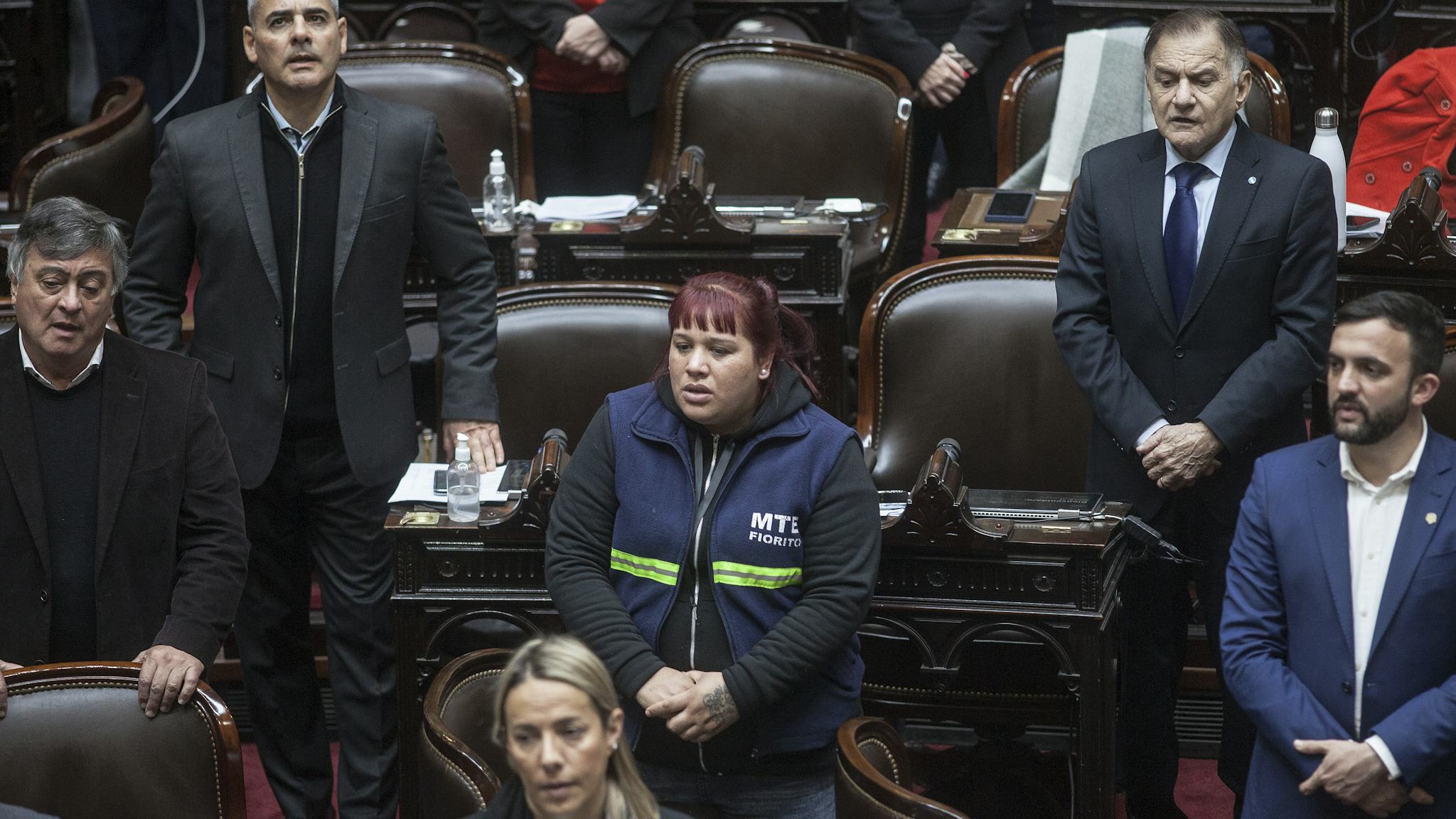 Natalia Zaracho sjunger nationalsången i Argentinas parlament. Hon bär arbetsuniform och är omgiven av parlamentariker i kostym.