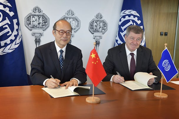 Kinas FN-ambassadör Chen Xu och ILO:s chef Guy Ryder undertecknar varsitt papper vid ett skrivbord.