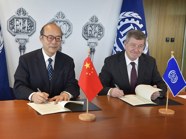 Kinas FN-ambassadör Chen Xu och ILO:s chef Guy Ryder undertecknar varsitt papper vid ett skrivbord.
