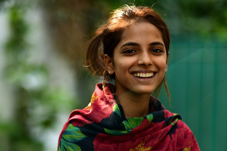 En ung pakistansk kvinna med färgglad sjal runt axlarna ler mot kameran.