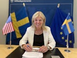 Anna Hallberg ler vid ett skrivbord, bredvid sig har hon svenska och amerikanska flaggor.