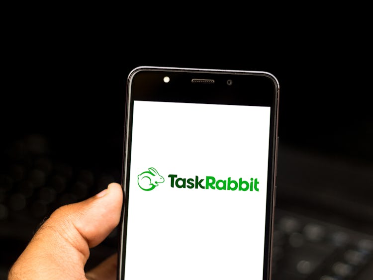 En hand håller upp en mobiltelefon, skärmen visar Taskrabbits logga.