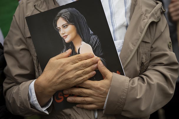 En man vars ansikte inte syns i bild trycker en bild av Mahsa Amini mot sitt bröst.