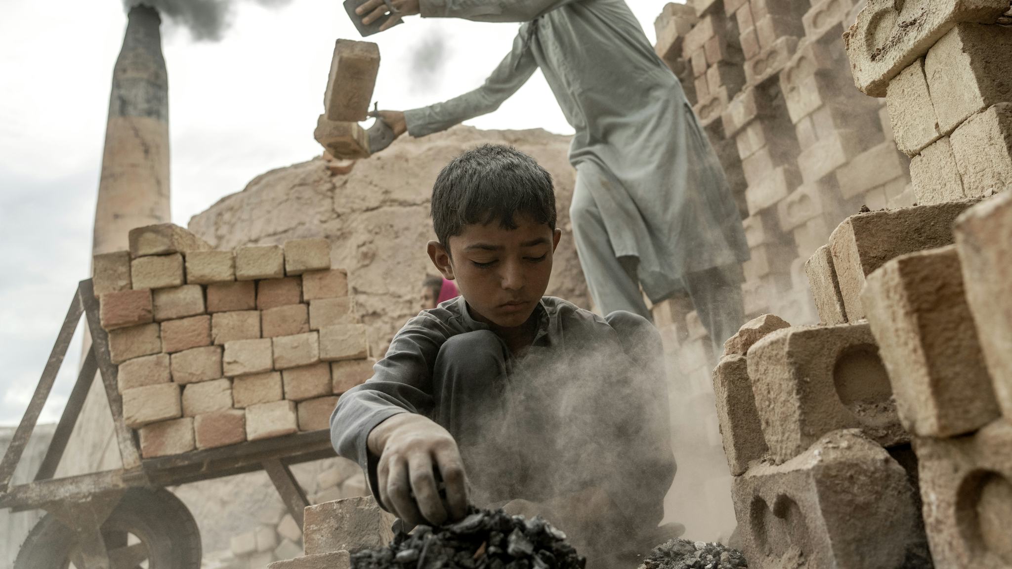 En barnarbetare jobbar i tegelfabriken i Afghanistan, i bakgrunden syns en vuxen arbetare.