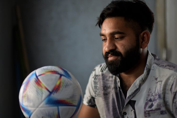 Bild på Ali Murtaza som tillverkar fotbollarna som ska användas under VM i Qatar. Han håller i en av VM-bollarna i handen.
