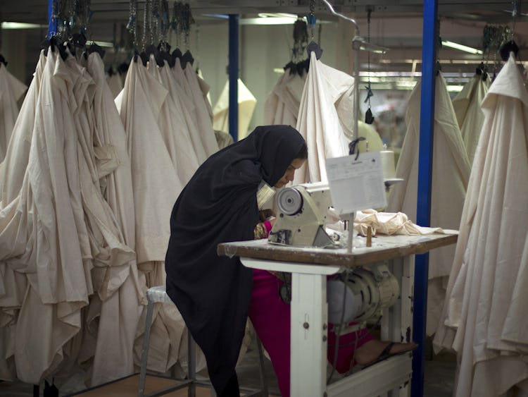 En kvinnlig textilarbetare i svart slöja syr kläder i Pakistan