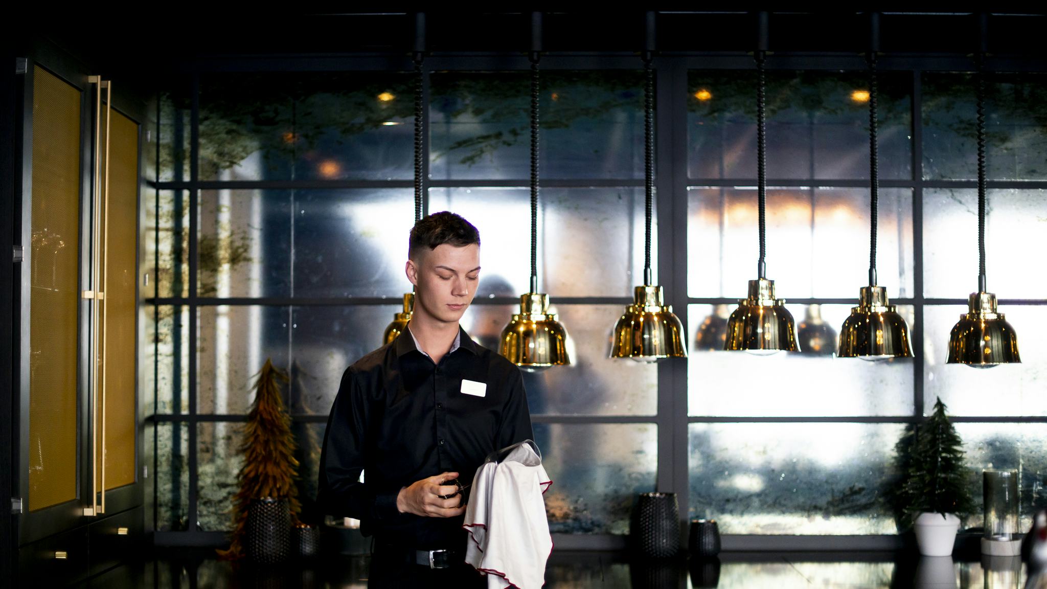 Gustav står i en restaurang där han jobbar och torkar ett glas.