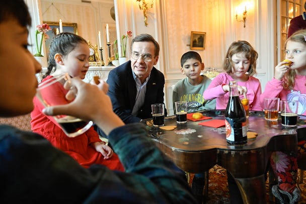 Ulf Kristersson och en grupp barn som sitter runt ett bord och dricker julmust.