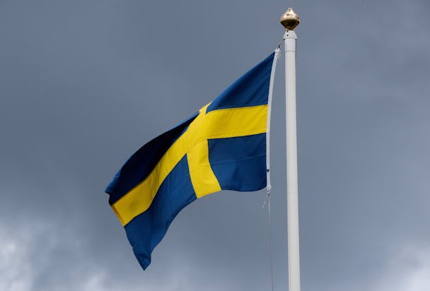 En svensk flagga vajar framför en molnig himmel.