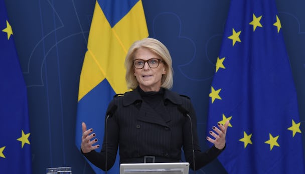 Elisabeth Svantesson står bakom ett podium framför EU- och svenska flaggor.