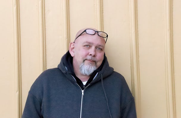 En skallig man med glasögon och en hoodie framför en gul vägg.