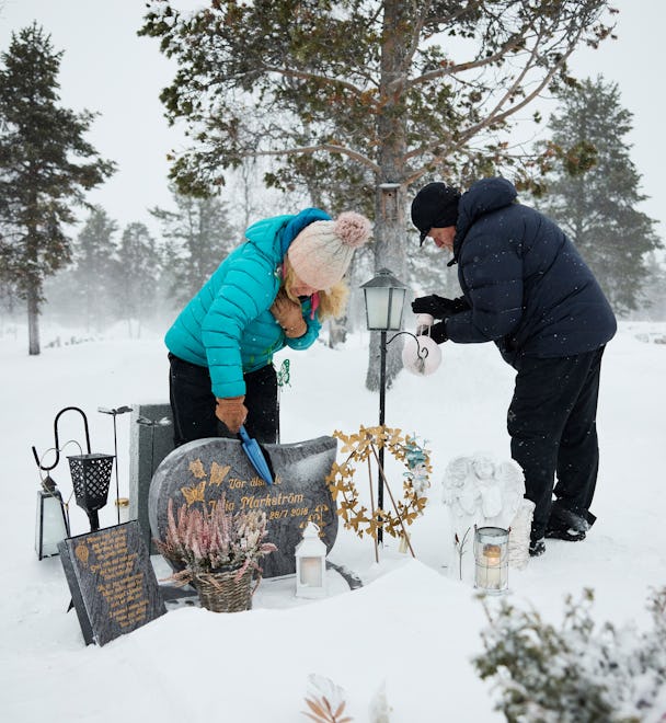 En man och kvinna lägger en krans på en grav i snön.