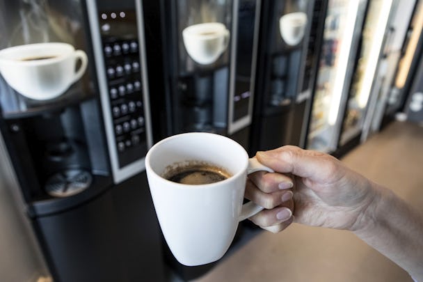 En persons hand som håller en nybryggd kopp kaffe från en maskin.