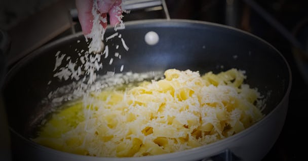 En hand strör riven ost över pastan i en kastrull.