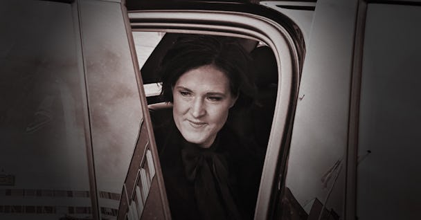 En kvinna klädd i svart sitter i baksätet i en bil, synlig genom en öppen dörr.
