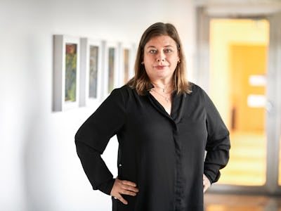 Malin Ragnegård, Kommunals ordförande, i svart blus står i ett konstgalleri med händerna på höfterna, med inramade bilder som hänger på väggen bakom henne.