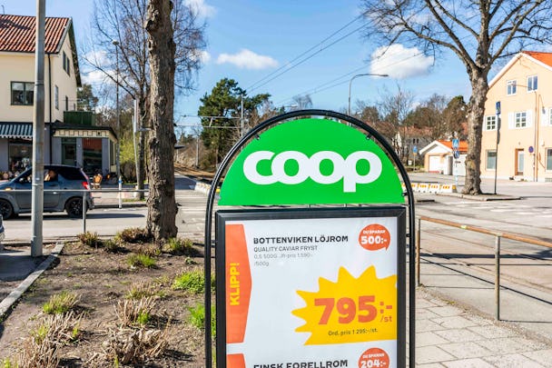 En coop stormarknad skylt som visar produktpriser, med en gata och byggnader synliga i bakgrunden.