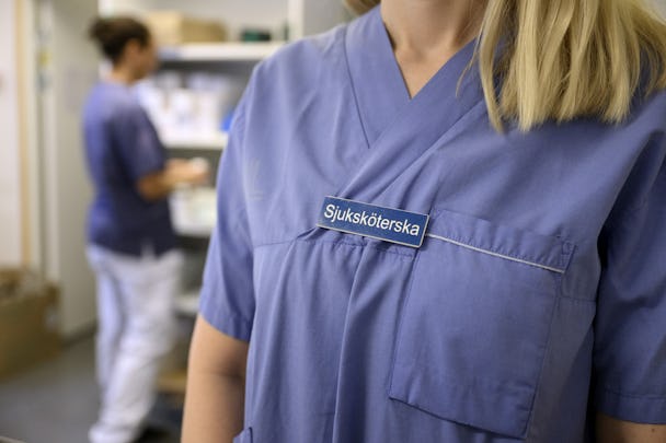 En person med namnskylt märkt "sjuksköterska", befinner sig i en sjukhusmiljö.