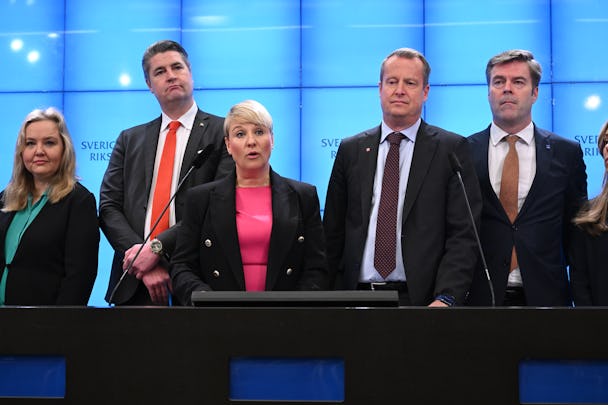Fem personer står bakom ett podium. De är klädda i formella kläder, och bakom dem finns en blå vägg med texten "Sveriges Riksdag.