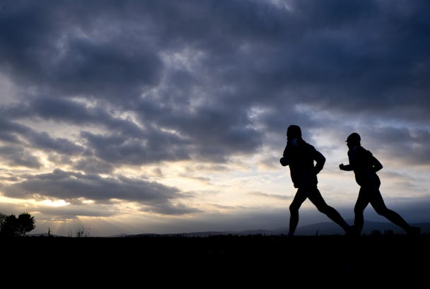 Två personer springer bredvid varandra som siluetter mot en molnig himmel vid gryning eller skymning.