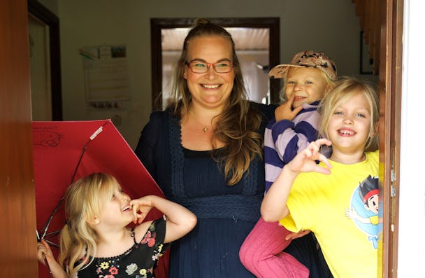 En kvinna står i en dörröppning och ler mot kameran, tillsammans med tre barn.