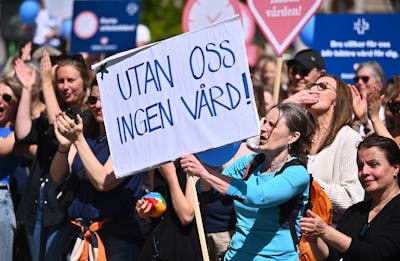 En grupp människor på en demonstration. En kvinna längst fram håller upp ett plakat med texten "UTAN OSS INGEN VÅRD!".