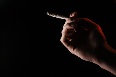 Närbild av en hand som håller en delvis rökt joint mot en mörk bakgrund.