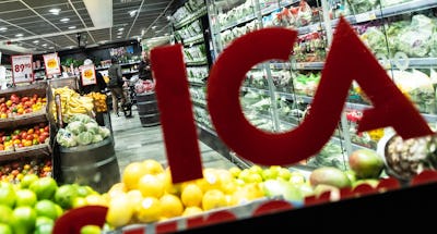 Vy från baksidan av en röd "ICA“-logotyp i en mataffär fylld med olika färska frukter och grönsaker.